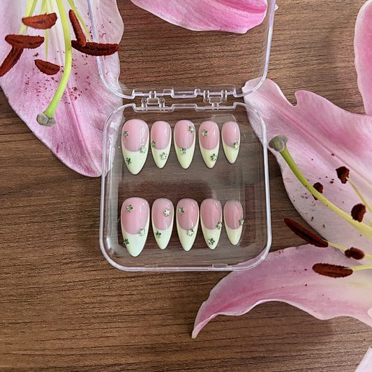 Set of pink and green nail art designs in a clear case on a wooden surface with pink lily flowers.
